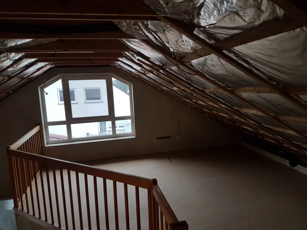 Dachboden vor dem Ausbau: offene Sparren mit alter Alufolie, Holzgeländer an der Treppe