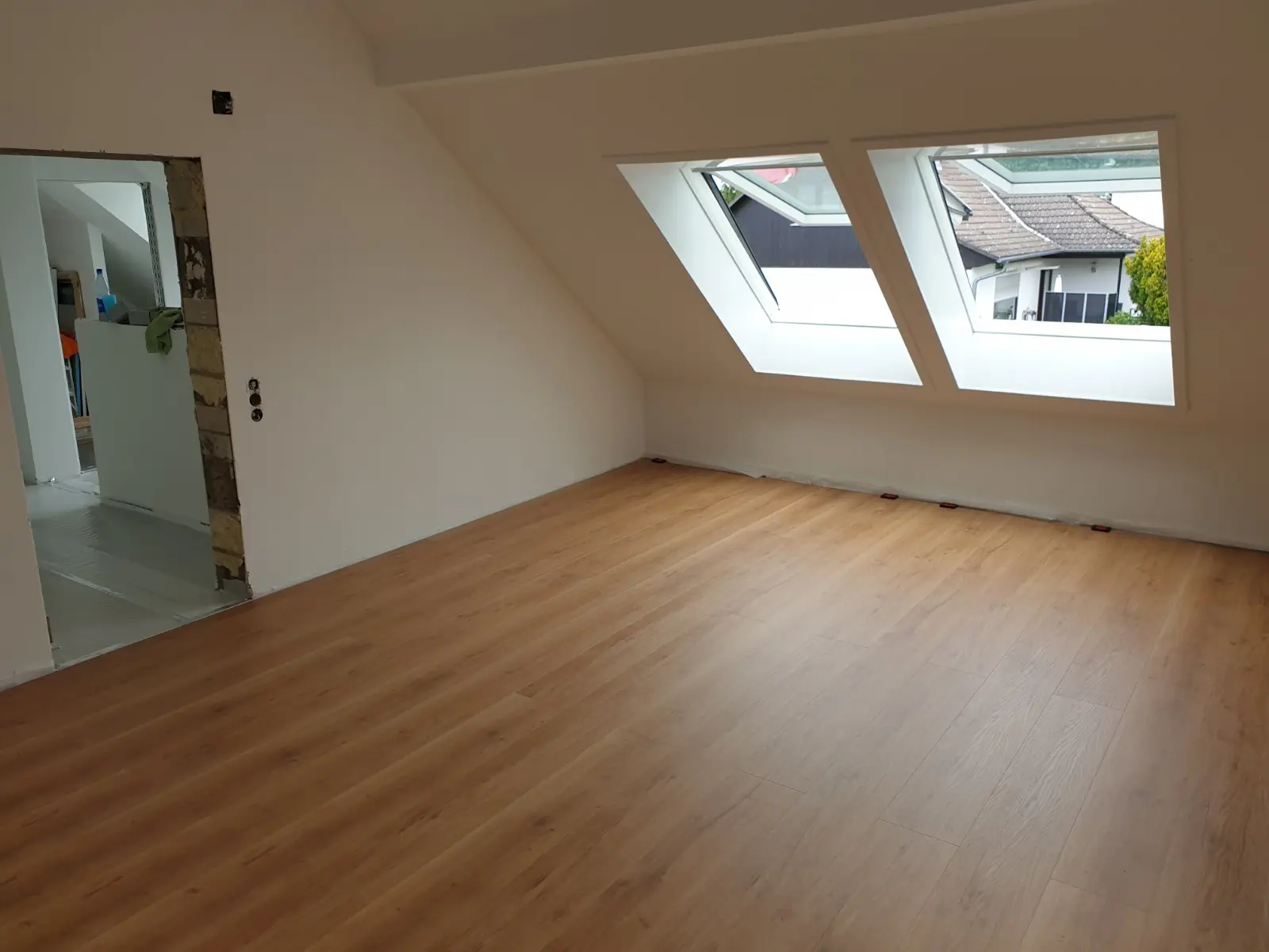 Von Olaf Schwarz ausgebautes Dachzimmer mit zwei Dachfenstern, weißen Schrägen und Holzboden